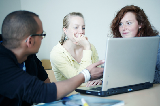 Drei junge Menschen diskutieren vor einem Laptop
