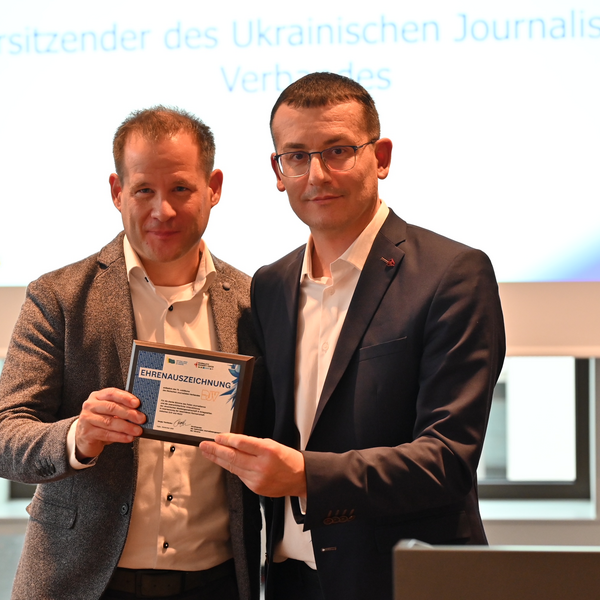 Sergiy Tomilenko überreicht Mika Beuster eine Ehrenauszeichnung für das starke Engagement des DJV für Pressefreiheit, auch und insbesondere in Kriegszeiten.